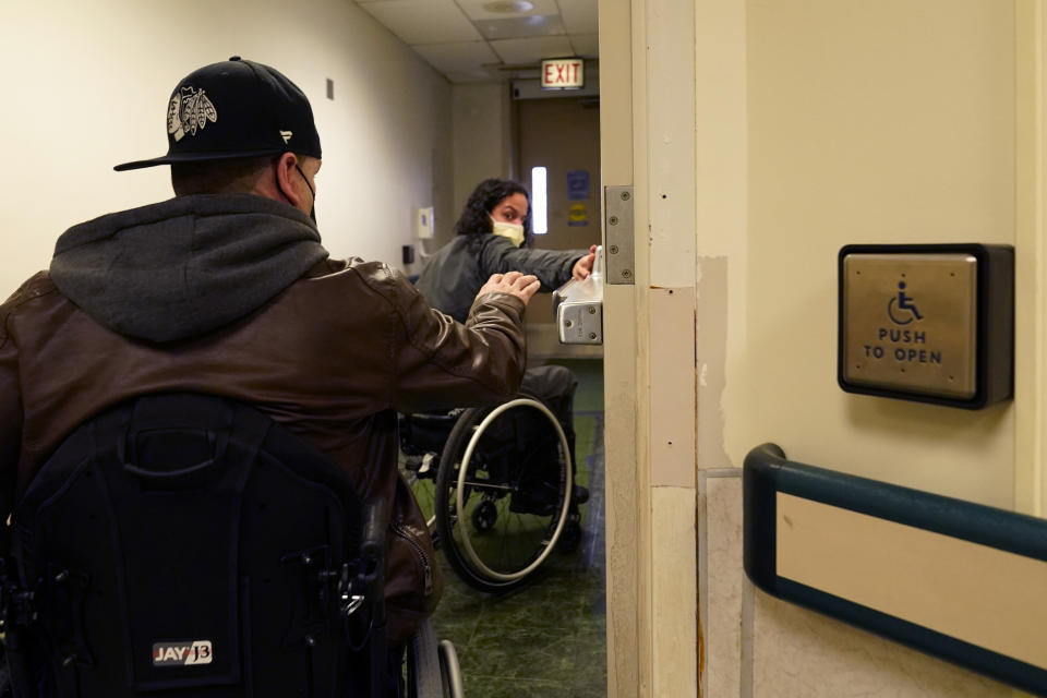 Jonathan Annicks, right, a part-time peer mentor for patients with spinal cord injuries at Schwab Rehabilitation Hospital, leads Cesar Romero out to Annick's car to teach him how to get in and out of a car and dismantle a wheel chair for driving Tuesday, March 29, 2022, in Chicago. "If he can do it, I can do it," said Romero, a 45-year-old Chicagoan who worked construction until he was shot and paralyzed last year while on his way to a grocery store. (AP Photo/Charles Rex Arbogast)