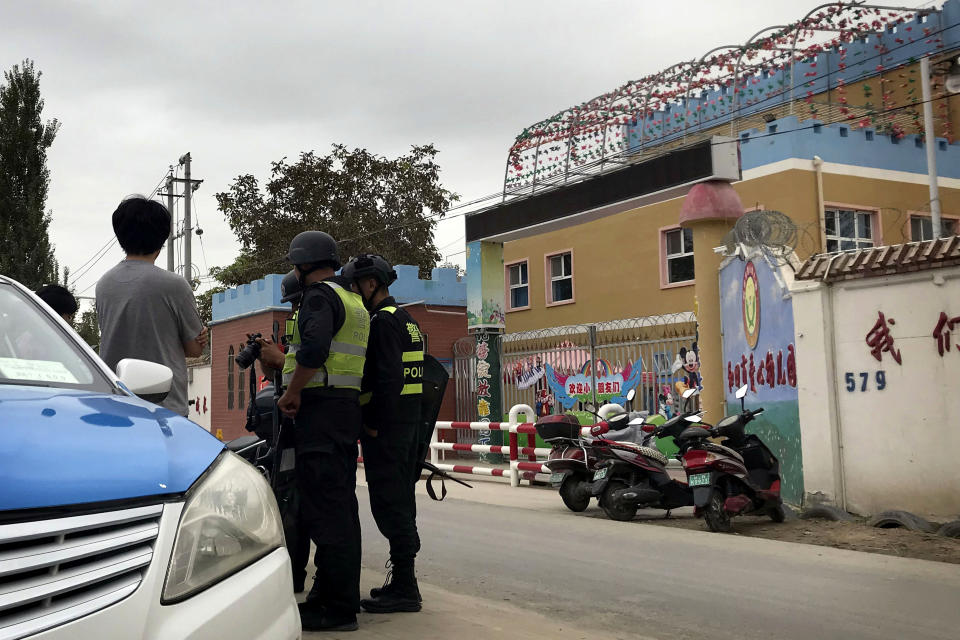 Policías apostados frente a un jardín de infantes de Hotan, en la región china de Xinjiang, revisan el equipo de un fotógrafo el 30 de agosto del 2018. Muchos hijos de musulmanes están siendo alojados por la fuerza en jardines de infantes como este, según denuncias. (AP Photo/Ng Han Guan)