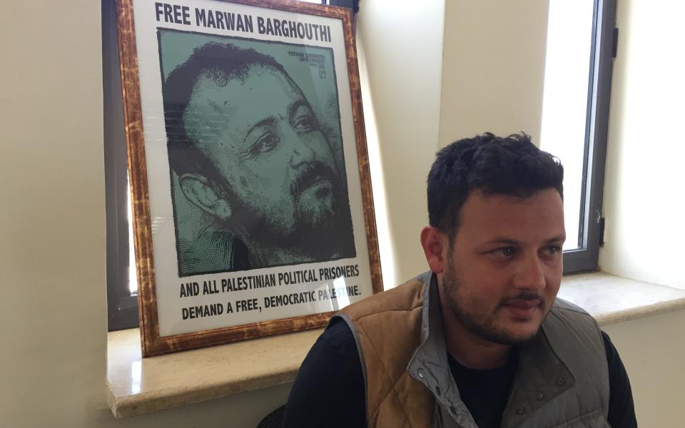 Qassam Barghouti sits in front of a poster of his father, Marwan Barghouti - Credit: Raf Sanchez