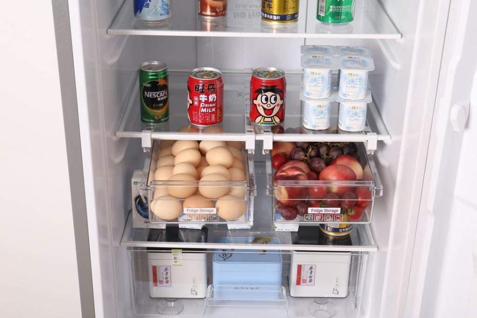 Interior of fridge showing plastic sliding storage trays holding eggs and fruit. Other shelves hold cans, yoghurt tubs etc.