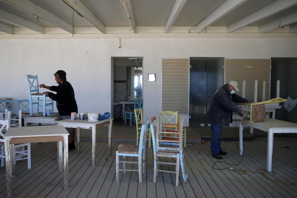 Workers paint the chairs of a tavern in Chora, on the Aegean island of Naxos, Greece, Tuesday, May 11, 2021. With debts piling up, southern European countries are racing to reopen their tourism services despite delays in rolling out a planned EU-wide travel pass. Greece Friday became the latest country to open up its vacation season as it dismantles lockdown restrictions and focuses its vaccination program on the islands. (AP Photo/Thanassis Stavrakis)