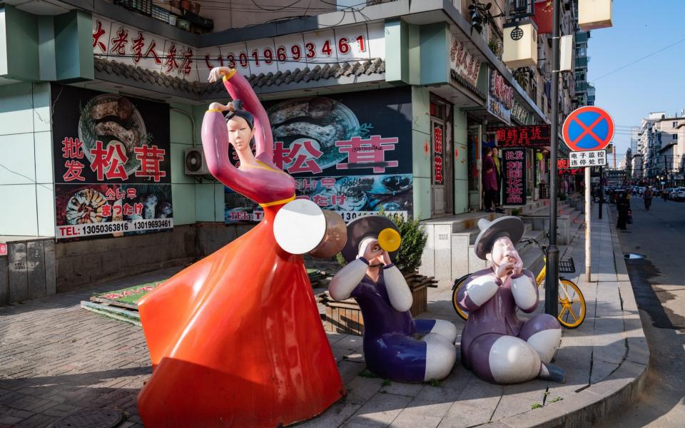 A statue of people dressed in traditional Korean clothes stands in a street full of shops that sell products from North and South Korea, in Dandong, China - Yan Cong for the Telegraph