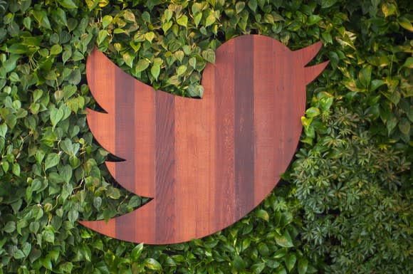 A wood-carved Twitter bird on a leafy background.