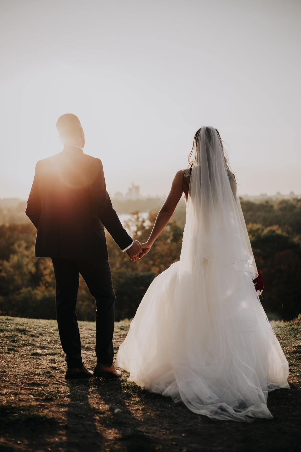 A couple holds hands and faces the sunset on their wedding day