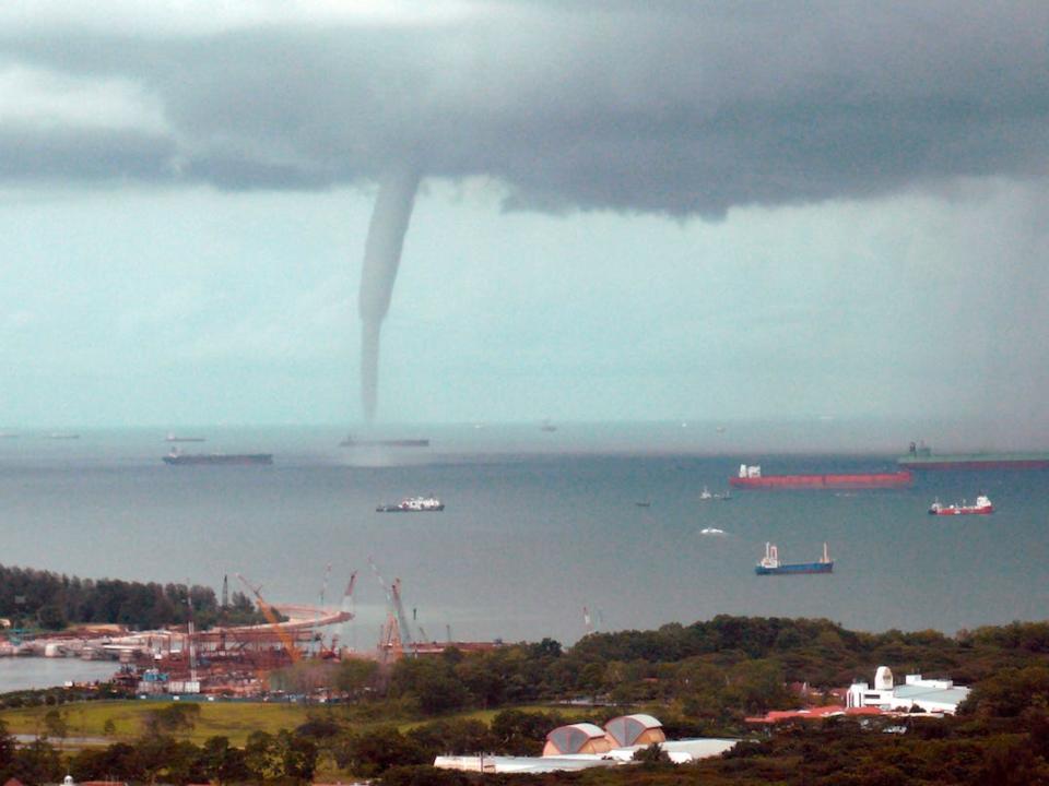 A funnel coming down from the clouds towards the earth seens to be sucking up water from a water source.