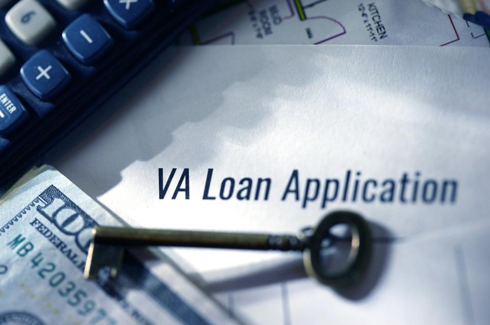 A close up of a document called 'VA loan application', sitting under a key, a $100 bill, and a calculator.