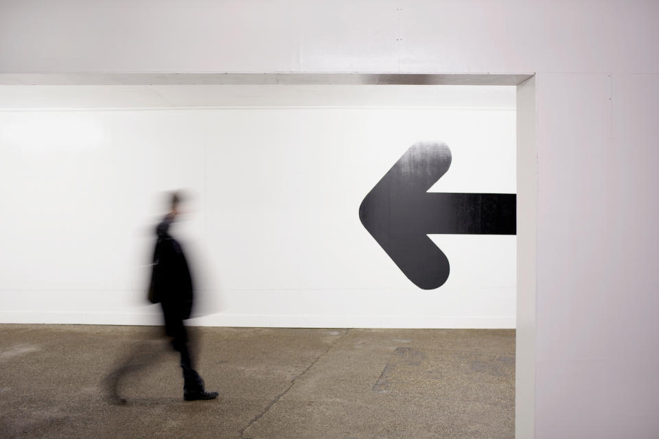 Person walking past a large arrow pointing left on a wall