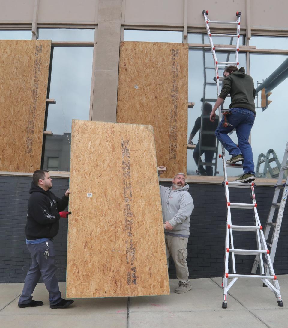 Chris Powell, left, and Jason Arnold, maintenance and safety director for Portage Path Behavioral Health Center, carry a sheet of plywood to board up the glass windows on East Exchange Street on Thursday, April 6, 2023 in Akron, Ohio. Fourteen windows were broken at the facility last July during the Jayland Walker protests costing the non-profit $32,000. "It was heartbreaking," said Arnold.