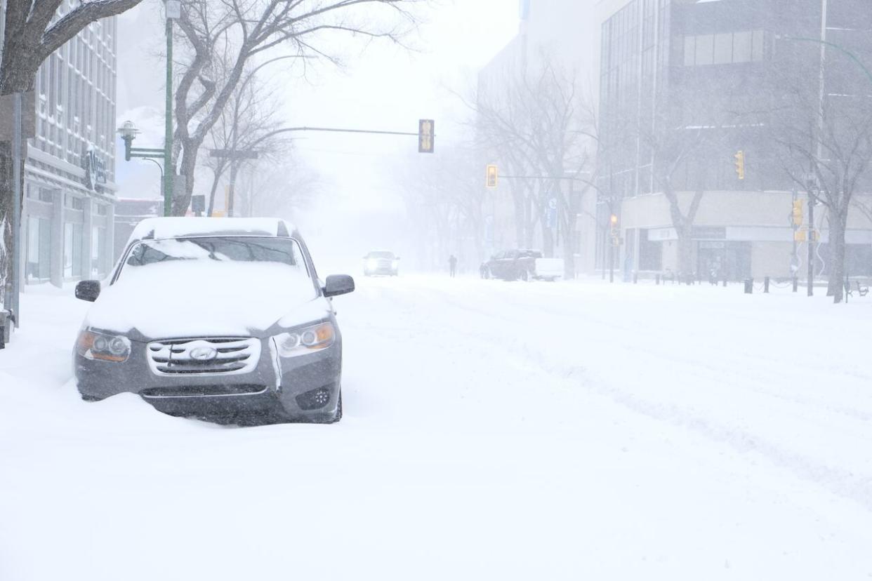 The winter storm is expected to bring up to 40 cm of snow to some areas of the province. In the photo, snow piles on top of a car in downtown Saskatoon as snow swirls around. (Liam O'Connor/CBC - image credit)