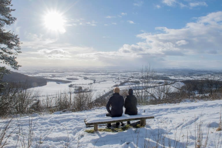 A couple sit on a bench overlooking the snow-covered fields of Thirsk in the North Yorks Moors National Park in North Yorkshire, on February 27, 2018