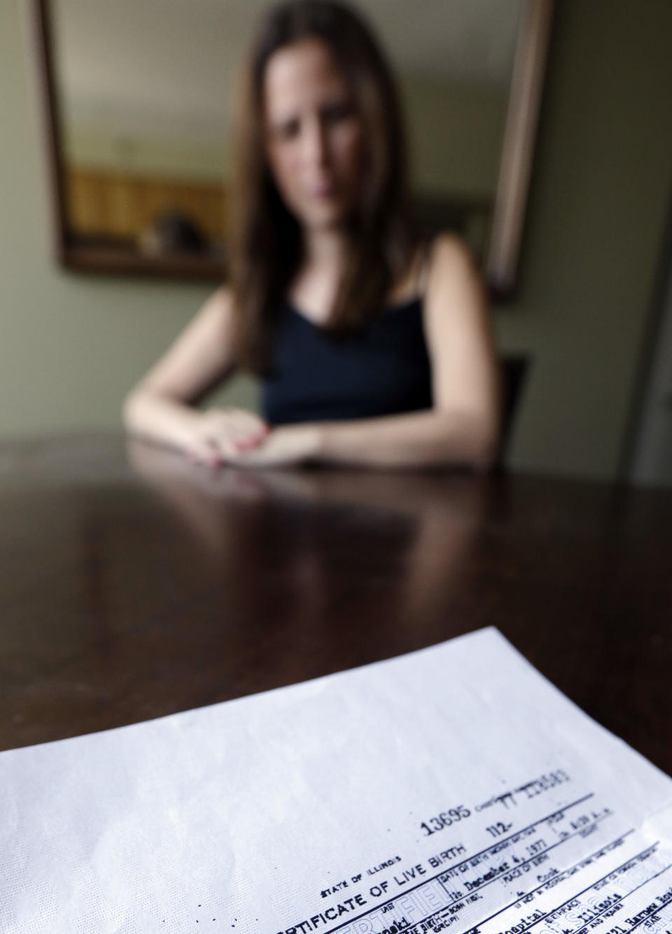 In this July 25, 2013 photo, Maura Duffy, 35, sits inside her apartment with her original birth certificate in Chicago. Duffy, who was adopted at birth, is among 8,800 Illinois residents since 2010 who have been able to see their original birth certificates, because of a law that opened documents sealed for decades. Duffy met her birth mother for the first time last September and says she is thankful to her birth mother and adoptive family for all they did for her. (AP Photo/Nam Y. Huh)