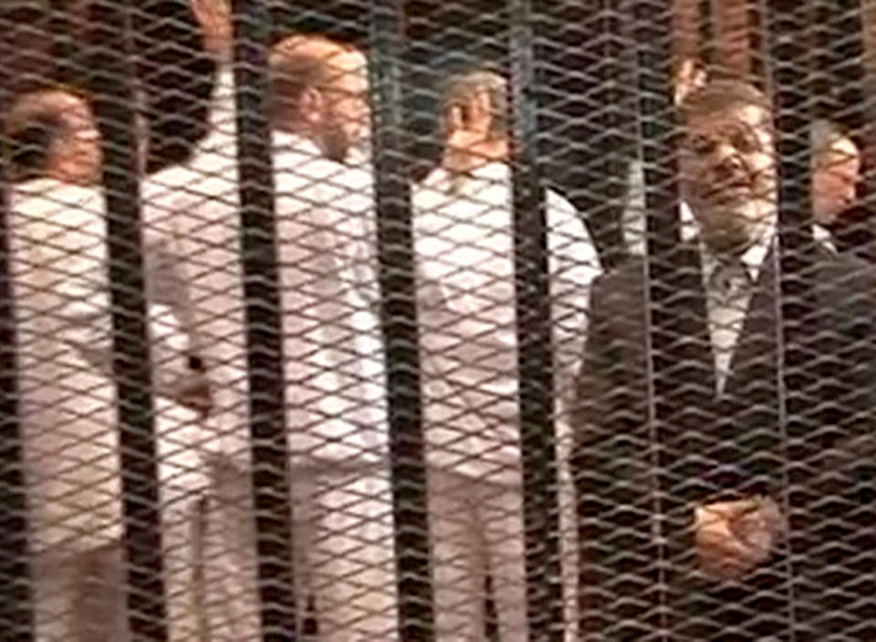 FILE - This Monday, Nov. 4, 2013 file image made from video provided by Egypt's Interior Ministry shows ousted President Mohammed Morsi, right, speaking from the defendant's cage as he stands with co-defendants in a makeshift courtroom during a trial hearing in Cairo, Egypt. Egypt’s crackdown on Islamists has jailed 16,000 people over the past eight months in the country’s biggest round-up in nearly two decades, according to previously unreleased figures from security officials. Rights activists say reports of abuses in prisons are mounting, with prisoners describing systematic beatings and miserable conditions for dozens packed into tiny cells. (AP Photo/Egyptian Interior Ministry, File)