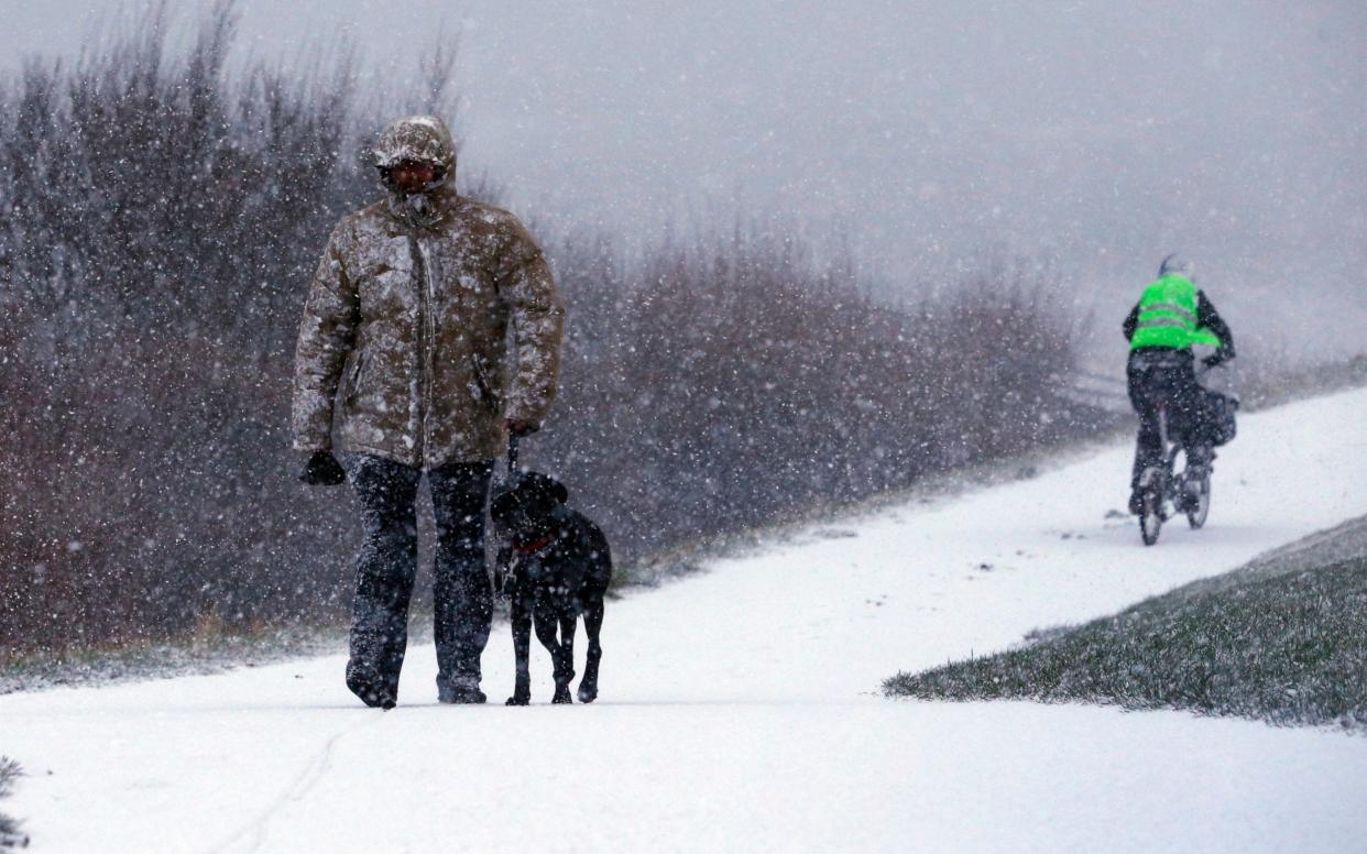 A man walks his dog through the snow in Whitley Bay, North Tyneside - PA