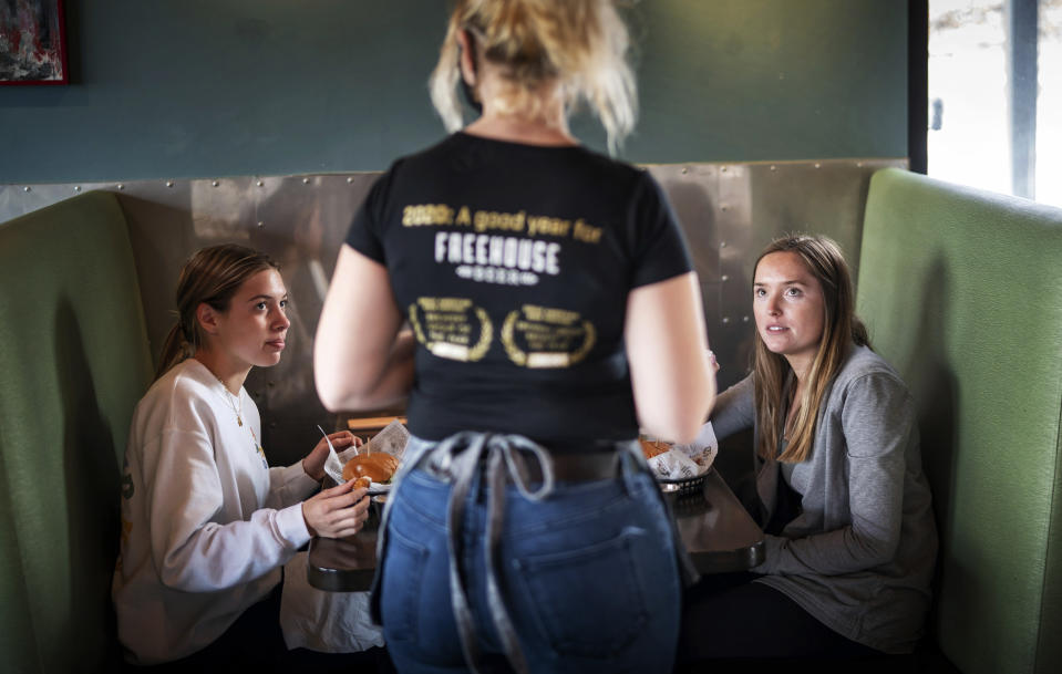 CORRECTS SPELLING OF FIRST NAME TO LINDSEY INSTEAD OF LUNDSEY - FILE - In this Jan. 11, 2021, file photo, Grace Mathre, server at Longfellow Grill, checks on University of St. Thomas students Lindsey Schulz and Maren Daggett in Minneapolis. As the U.S. finds itself in the most lethal phase of the coronavirus outbreak yet, governors and local officials in hard-hit parts of the country are showing little willingness to impose any new restrictions on businesses to stop the spread. (Glen Stubbe/Star Tribune via AP, File)