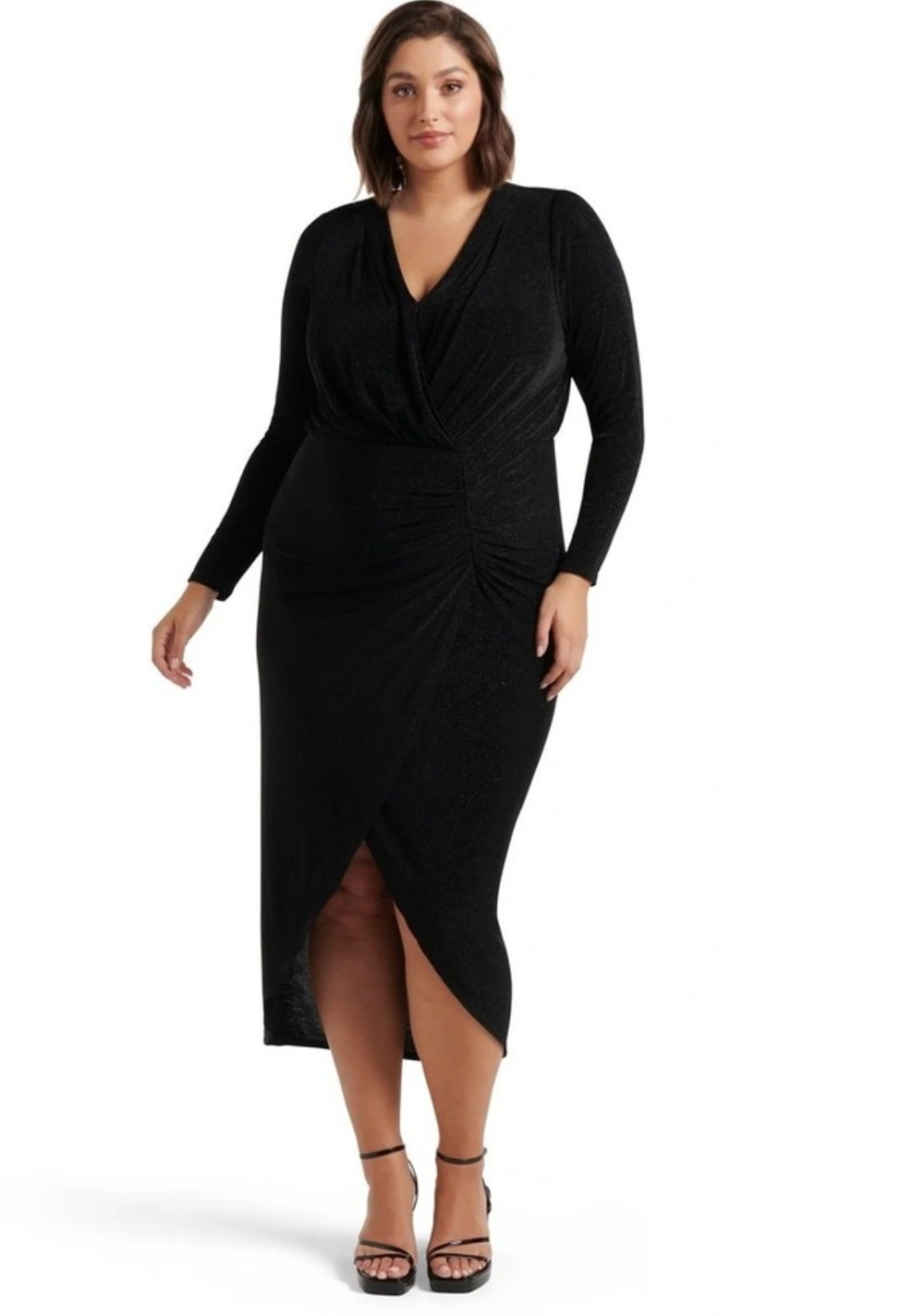 A large size model wears a dark tight-fitting wrap dress with long sleeves, with high heels.