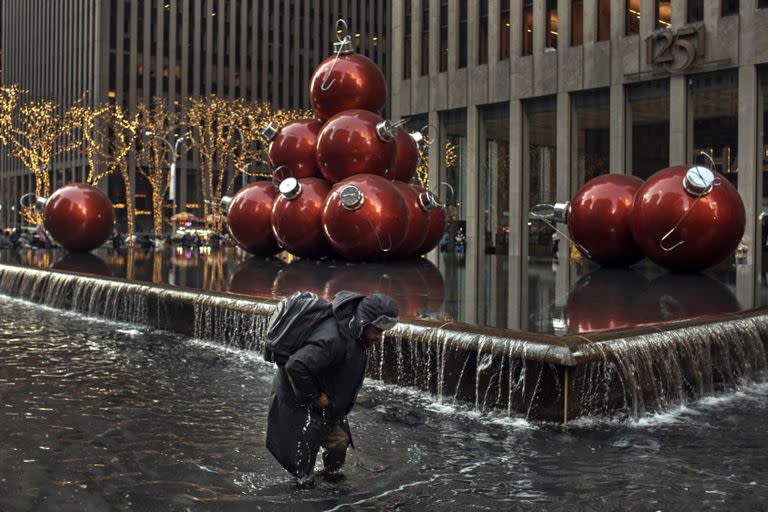 Un hombre recoge monedas caminando dentro de una fuente con agua helada el día de Navidad, en medio de las tormentas de nieve, el domingo 25 de diciembre de 2022, en Nueva York.