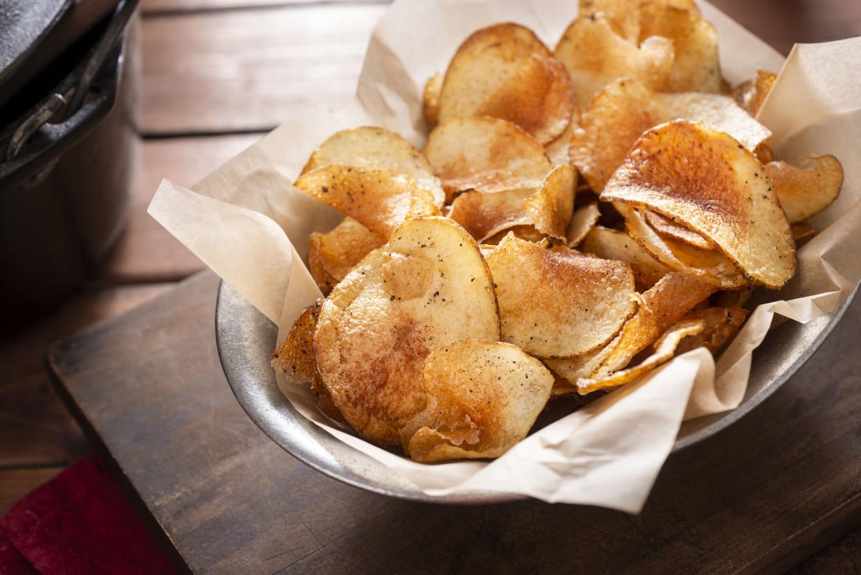 A bowl of homemade potato chips on a wooden cutting board on a wooden table