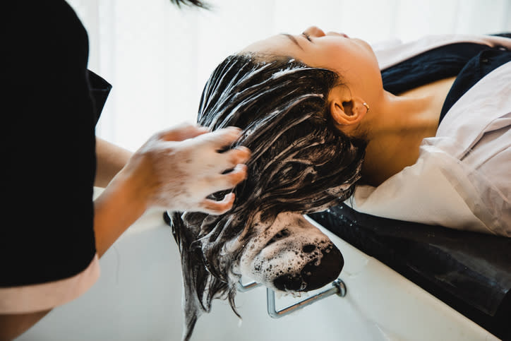 Person getting their hair shampooed at a salon, reclining with eyes closed as a stylist works