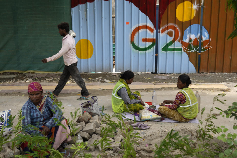 Laborers take a lunch break near a construction site covered with G20 summit logo in New Delhi, India, Thursday, Aug. 24, 2023. As India gears up to host the annual gathering of the Group of 20 industrialized and developing nations, the capital city is undergoing an elaborate makeover. But for many street vendors and shantytowns dotting the city, the beautification of New Delhi has meant displacement and loss of livelihoods. (AP Photo/Manish Swarup)