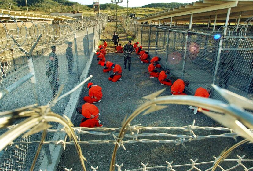 In this photo released 18 January 2002 by the Department of Defense, Al-Qaeda and Taliban detainees in orange jumpsuits sit in a holding area under the surveillence of US military police at Camp X-Ray at Naval Base Guantanamo Bay, Cuba, during in-processing to the temporary detention facility 11 January 2002. The detainees, captured in Afghanistan during Operation Enduring Freedom, are given a basic physical exam by a doctor, to include a chest x-ray blood samples drawn to assess their health. AFP PHOTO / US NAVY / Shane T. McCOY (Photo by - / DOD / US NAVY / AFP) (Photo by -/DOD / US NAVY/AFP via Getty Images)
