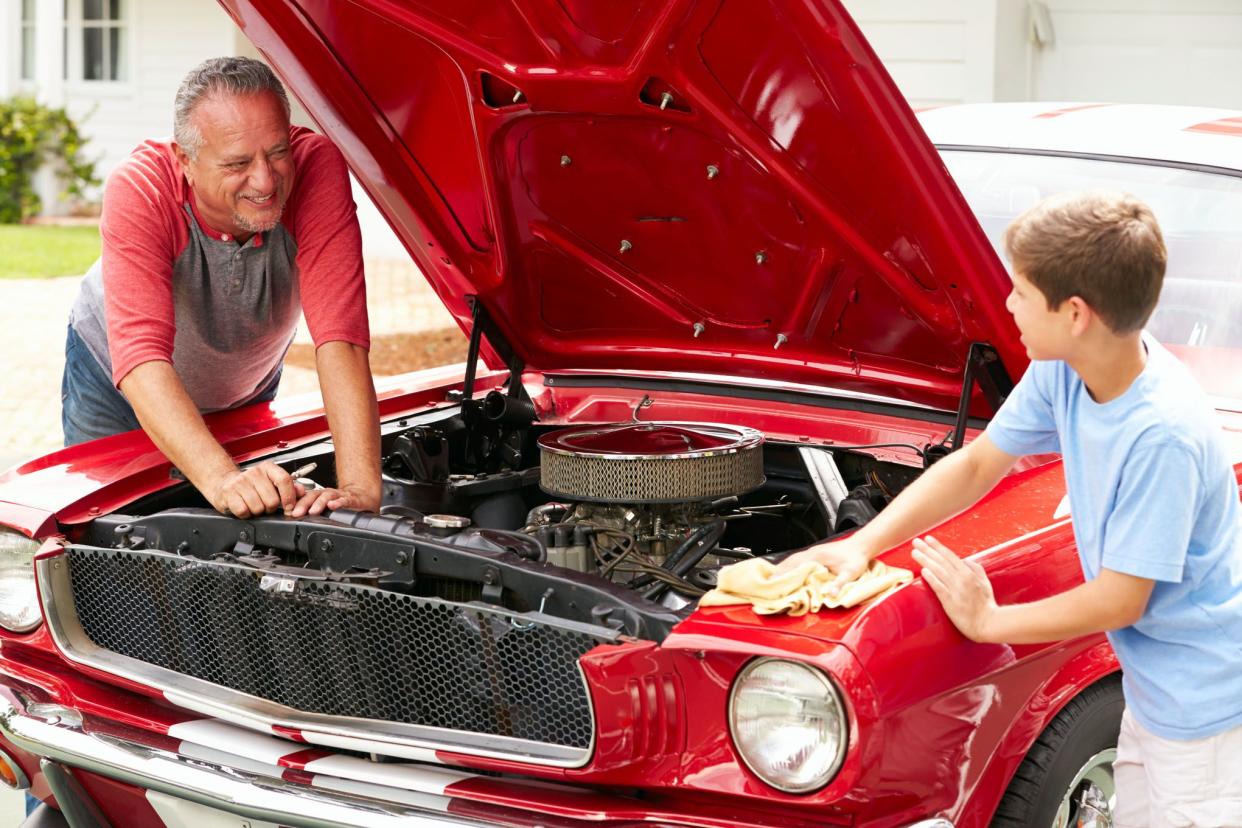 man and boy working on car under hood, smiling