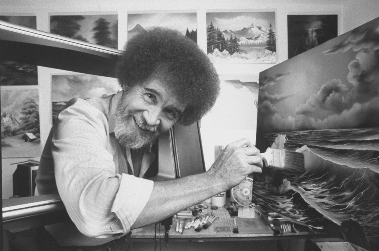 TV painting instructor/artist Bob Ross using a large paint brush to touch up one of his large seascapes in his studio at home.