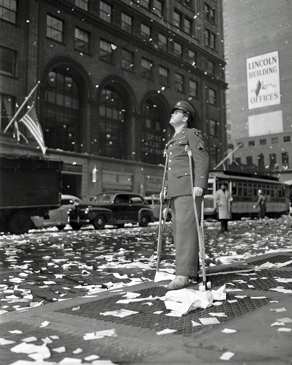 FILE - In this May 7, 1945 file photo Staff Sgt. Arthur Moore of Buffalo, N.Y., who was wounded in Belgium, stands on 42nd Street near Grand Central Station in New York as New Yorkers celebrate news of the surrender of Germany in World War II. Nazi commanders signed their surrender to Allied forces in a French schoolhouse 75 years ago this week, ending World War II in Europe and the Holocaust. Unlike the mass street celebrations that greeted this momentous news in 1945, surviving veterans are marking V-E Day this year in virus confinement, sharing memories with loved ones, instead of in the company of comrades on public parade. (AP Photo)