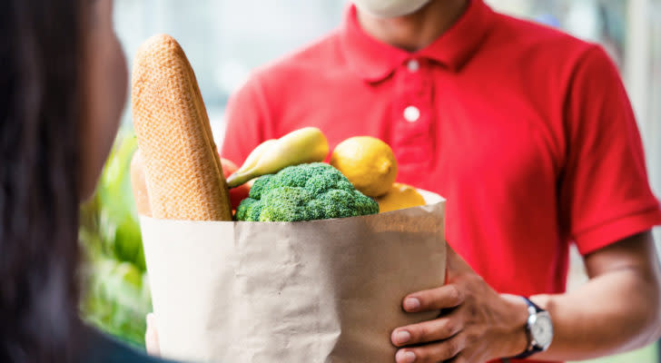 A person receives a delivery of groceries in a paper bag from other person.