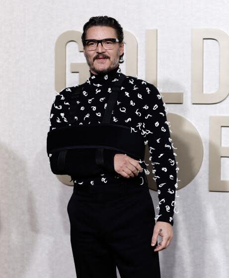 Pedro Pascal in thick eyeglasses in a black mesh shirt with white thread decoration and black pants posing at a red carpet