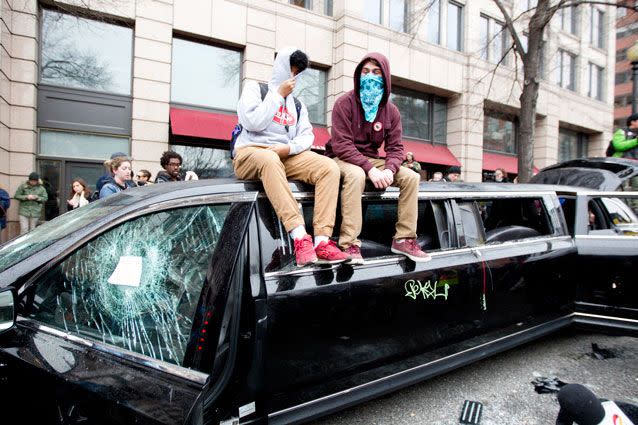 Demonstrators hide their faces while sitting  on a limousine with the windows broken during the demonstration. Source: AP