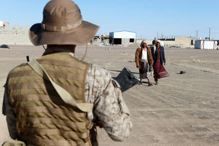 Yemeni people walk past a Saudi soldier standing guard during the delivery of oil tanker trucks by Saudi authorities to support charities and NGOs in Marib, Yemen January 26, 2018. Picture taken January 26, 2018. REUTERS/Faisal Al Nasser