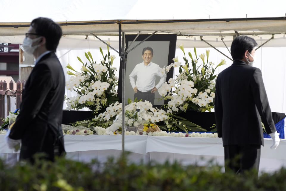 Staff stand near a flower offering stand for former Prime Minister Shinzo Abe, at Zojoji temple prior to his funeral wake Monday, July 11, 2022, in Tokyo. Abe was assassinated Friday while campaigning in Nara, western Japan. (AP Photo/Eugene Hoshiko)