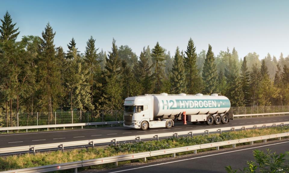 A hydrogen transport truck on a freeway beside an evergreen forest.