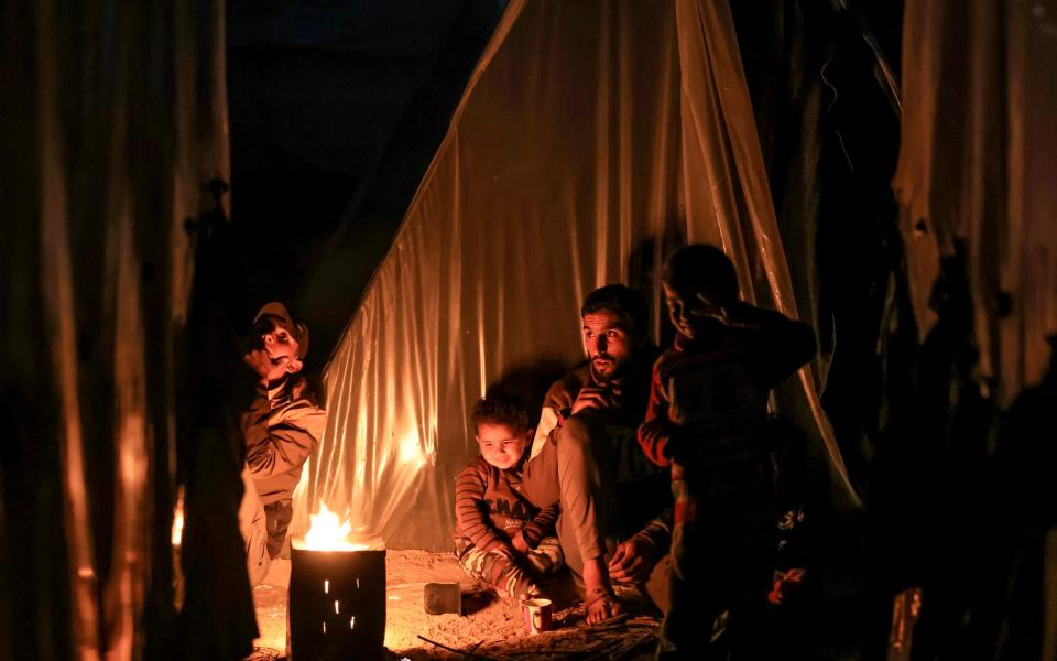 A man sits with children by a fire outside one of the tents housing Palestinians  in Rafah