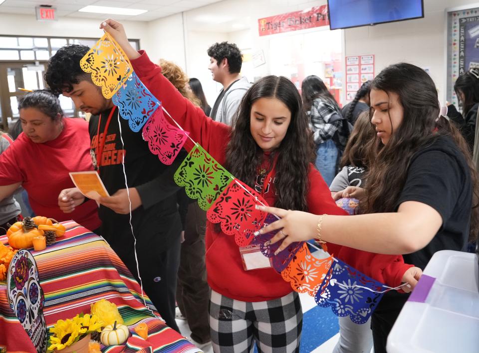 Des Moines East High juniors Melissa Perez, center, and Giselle Renteria, right, help elementary students hang up papel picado on an ofrenda near the entrance at Capitol View Elementary School in Des Moines on Tuesday, Oct. 25, 2022.