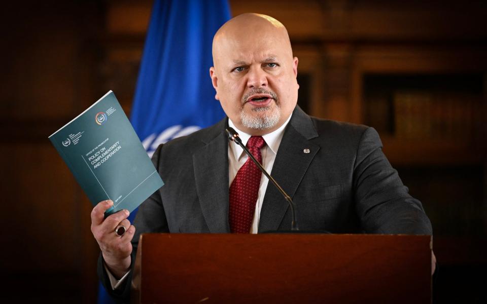 Karim Khan KC holds aloft a pamphlet and speaks at a lectern