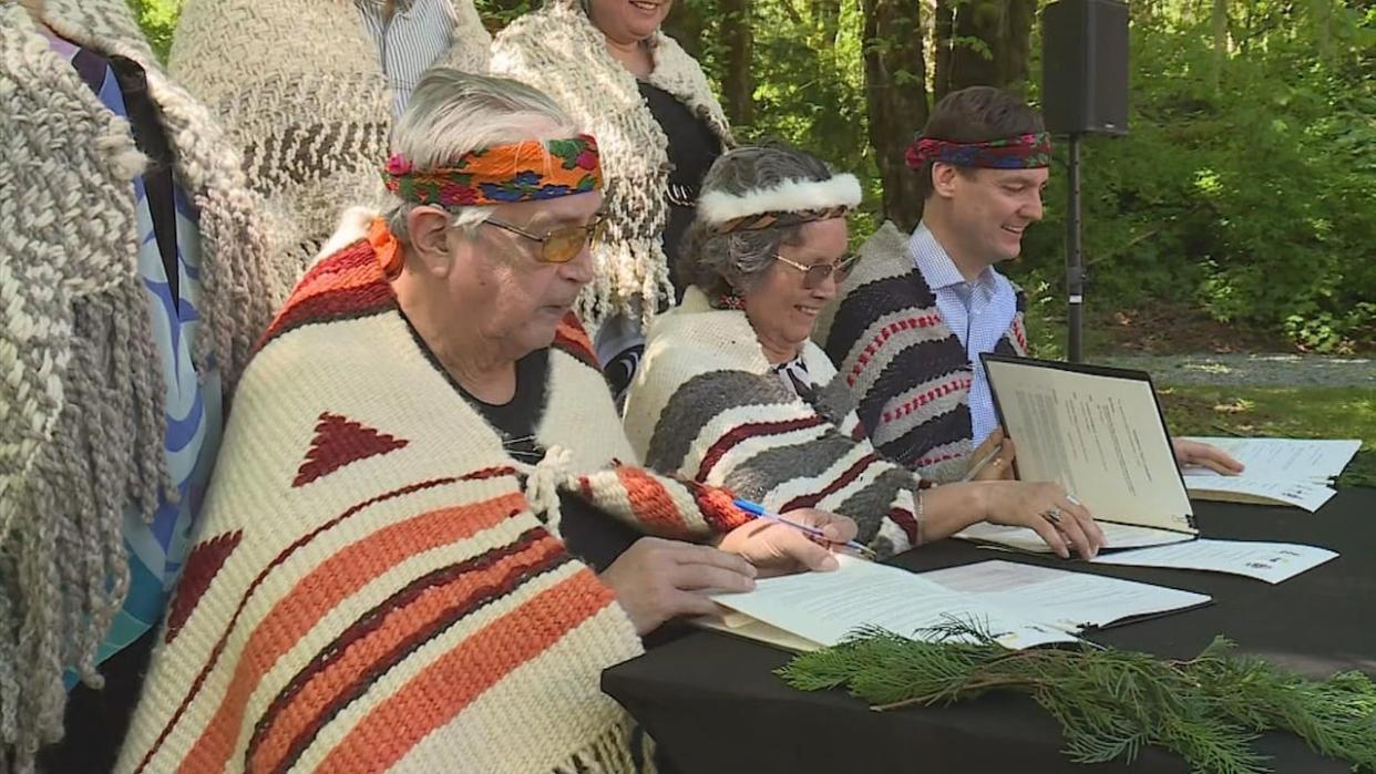 Lyackson First Nation Chief Pahalicktun, left, Cowichan Tribes Chief Cindy Daniels, centre, and B.C. Premier David Eby sign an incremental treaty agreement to transfer 312 hectares of land to the two Nations. (Dean Stoltz/CHEK News - image credit)