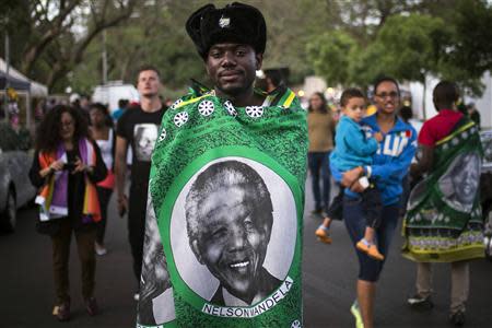 Hamza Massengo from the Republic of the Congo covers himself with an image of Nelson Mandela amid a crowd of mourners gathered outside the Mandela house in the Houghton Estates neighborhood of Johannesburg, South Africa December 7, 2013.REUTERS/Adrees Latif