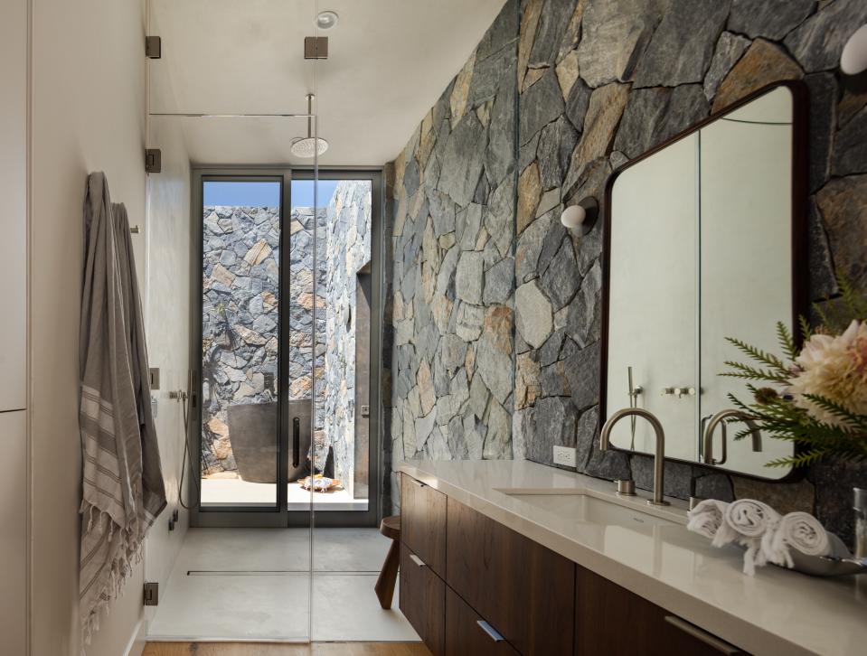 A Mediterranean-inspired flagstone wall unifies indoor and outdoor in the main bathroom. Past a floor-to-ceiling glass wall and All Weather sliding doors, a soaking tub occupies the private courtyard.