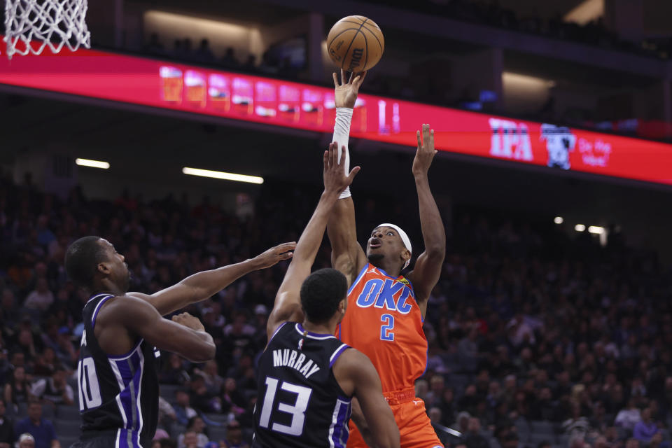 Oklahoma City Thunder guard Shai Gilgeous-Alexander (2) shoots against Sacramento Kings forwards Keegan Murray (13) and Harrison Barnes (40) during the second half of an NBA basketball game in Sacramento, Calif, Thursday, Dec. 14, 2023. (AP Photo/Jed Jacobsohn)