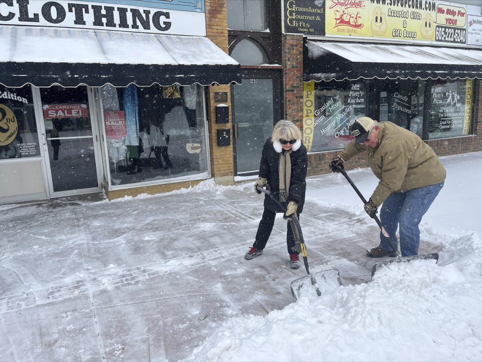 Carolyn and Dan Ellwood shovel snow outside Second Edition in Pierre, S.D. on Wednesday, Feb. 22, 2023. Brutal winter weather hammered the northern U.S. Wednesday with “whiteout” snow, dangerous wind gusts and bitter cold, shutting down roadways, closing schools and businesses and prompting dire warnings for people to stay home. (AP Photo/Amancai Biraben)