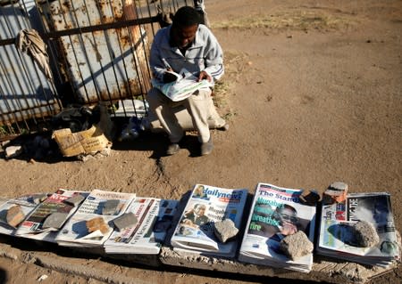 A newspaper vendor waits for customers along a street in Highfields