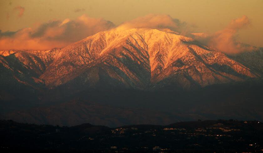 The setting sun casts a golden glow on the snow-covered peaks of Mt. Baldy.
