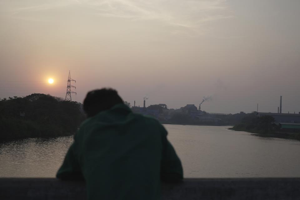 A man watches the sun as it sets over the chemical industries located along the banks of the Periyar River in Eloor, Kerala state, India, Saturday, March 4, 2023. Residents have risen up against the factories contaminating the river in the area. (AP Photo)