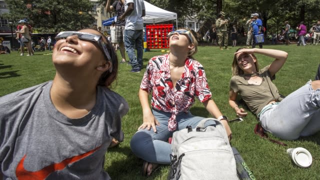 Women sit in a park to view the solar eclipse with glasses on