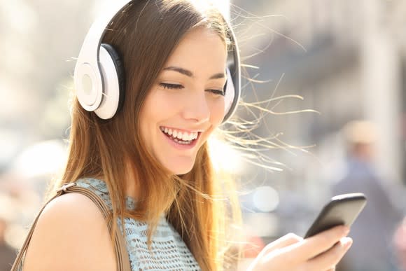 Smiling young woman with white headphones on while looking at her smartphone