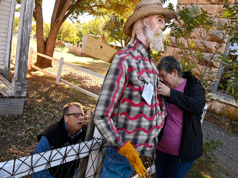 Scott Clowdus and Holly Woodard fasten a scarecrow representing Big Country artist Chuck Roach to the fence surrounding the Hill House at Buffalo Gap Historic Village Wednesday.