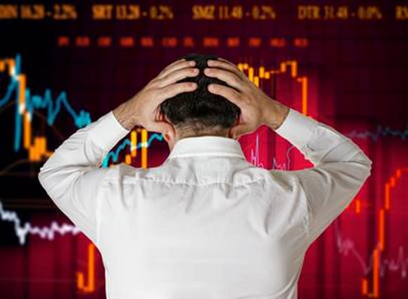 A person looking at a declining stock price chart holds his head with his hands.