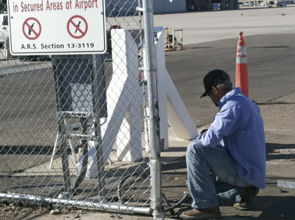 An unidentified worker makes repairs to a gate at Phoenix Sky Harbor International Airport Friday morning, Nov. 16, 2012, after a woman driving with a small child in her car crashed through the gate and drove on a runway Thursday night. The incident was the latest in a series of similar mishaps across the country that have raised questions whether the nation's airports are truly secure. (AP Photos/Jacques Billeaud)