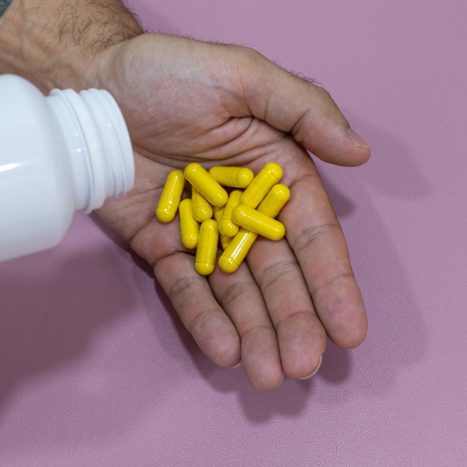 A close up of a man's hand holding bright yellow pill capsules.